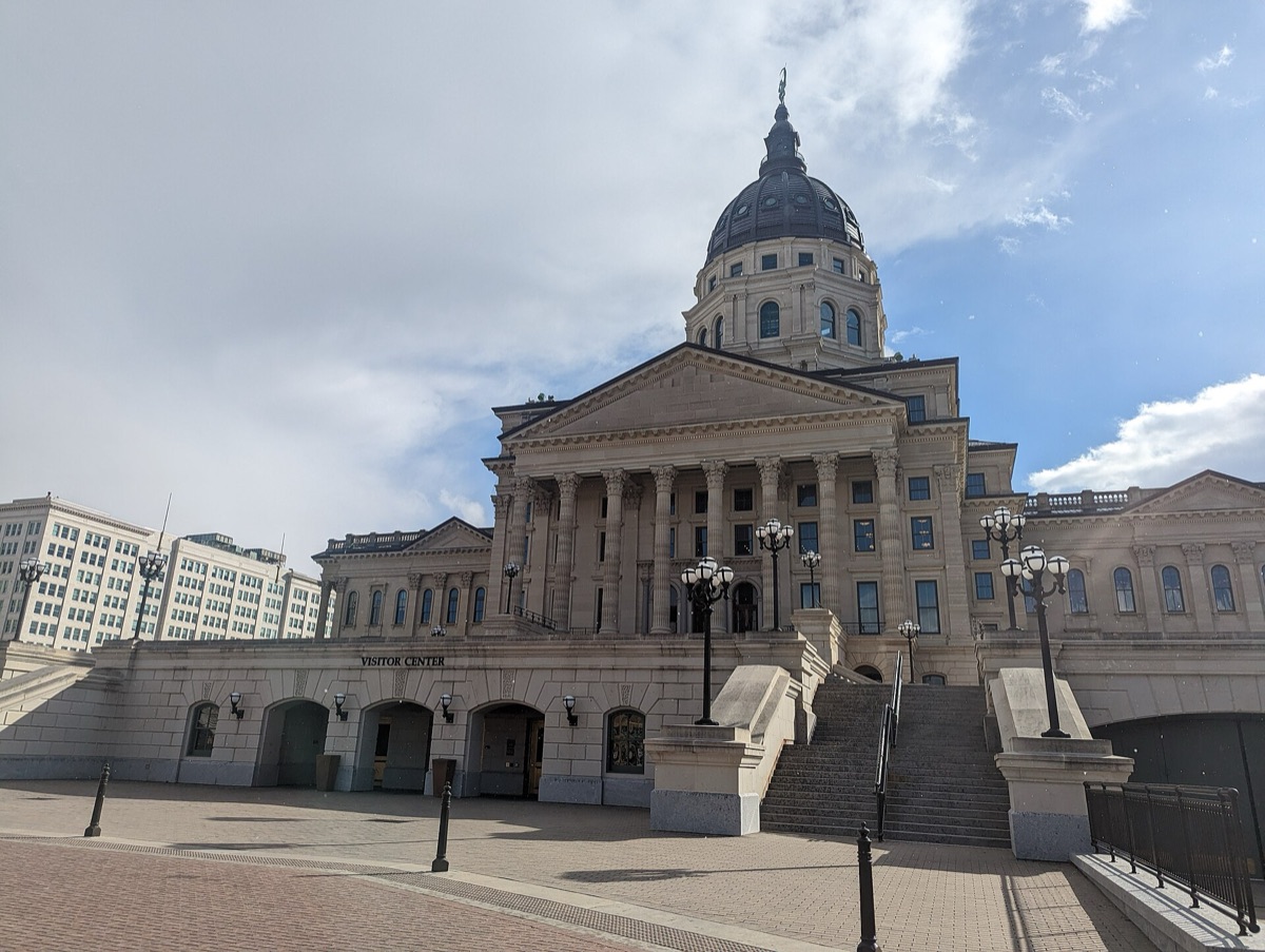 The Kansas State Capitol building and dome in Topeka beneath a partly cloudy sky.